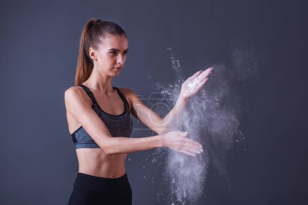 Foto de Hermosa chica en ropa deportiva está utilizando talco en polvo para sus manos, sobre fondo gris - Imagen libre de derechos