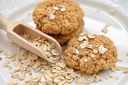 Oatmeal cookies with wooden scoop and oat flakes on a white plate. Healthy food for breakfast or a snack