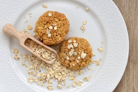 Oatmeal cookies with wooden scoop and oat flakes on a white plate. Healthy food for breakfast or a snack. Top view