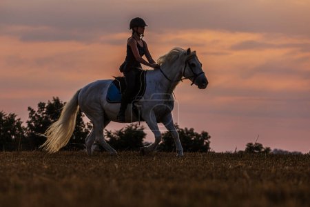 une femme qui monte à cheval au crépuscule