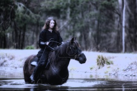 Photo for Black dressed woman in historical sitting on a horse that's on its hind legs in the lake - Royalty Free Image