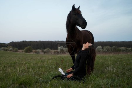 Foto de Mujer vestida de negro con un arco y flecha sentado debajo de un caballo - Imagen libre de derechos