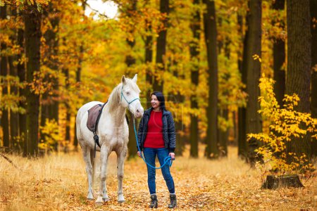 Foto de Una joven y un caballo blanco caminan por un sendero forestal. - Imagen libre de derechos