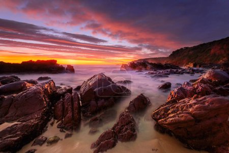 Foto de Salida del sol rojo vivo sobre la costa rocosa de la playa - Imagen libre de derechos