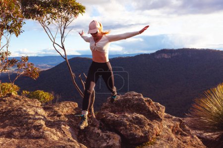 Woman jumping stride off rocks at cliff ledge with pretty  mountain and valley views