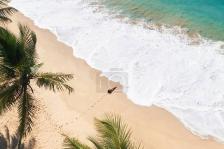 Téléchargez les photos : Vue aérienne sur drone belle plage tropicale avec des palmiers de sable blanc et de l'eau claire et modèle femme en bikini noir. Rivage parfait avec des palmiers de sable et de coco. Voyages et loisirs abstraits - en image libre de droit