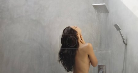 Foto de Vista posterior de una perfecta joven morena adulta con una figura perfecta tomando una ducha, salpicándose de agua. Foto de alta calidad - Imagen libre de derechos