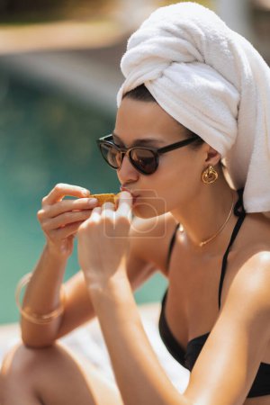 Téléchargez les photos : Une jeune femme en maillot de bain élégant et lunettes de soleil, mangeant des mangues pendant ses vacances d'été. Style de vie riche et insouciant - en image libre de droit