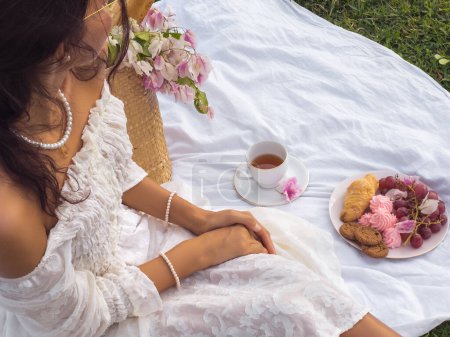 Téléchargez les photos : Une jeune femme jouissant d'un pique-nique romantique dans le parc, détails vintage et couverture boho, tasse à thé, assiette de friandises sucrées. - en image libre de droit