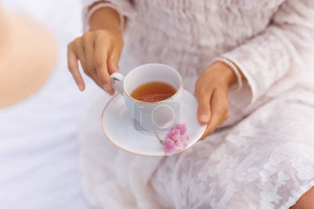 Foto de Una mujer se relaja al aire libre mientras sostiene una taza de té caliente, que proporciona refresco y relajación. - Imagen libre de derechos