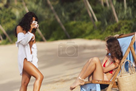 Foto de Una modelo joven y atractiva posa en un bikini glamoroso en la playa tropical para una sesión de fotos al aire libre. Tomar fotografías amateur con una cámara instantánea para capturar hermosos recuerdos de este romántico - Imagen libre de derechos