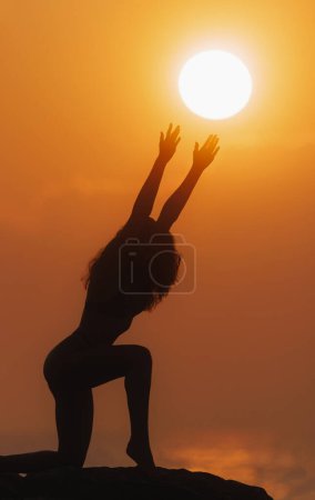 Photo for Full-length body silhouette of a young sporty woman doing yoga asasnas, morning stretching, a sun disk in her hands. Sport, religion and spirituality concept. - Royalty Free Image