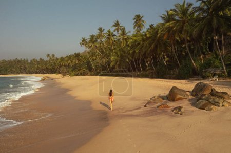 Téléchargez les photos : Vue aérienne par drone du modèle féminin de bikini en maillot de bain rouge se relaxant et marchant seul sur une incroyable plage de sable tropical. Voler haut au-dessus d'une fille touristique magnifique méconnaissable explorer un exotique - en image libre de droit