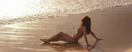 Foto de Seductora mujer de vacaciones en bikini de playa sentada en la playa en sensación de libertad, disfrutando de sus vacaciones de verano. Feminidad y belleza femenina foto de alta calidad - Imagen libre de derechos