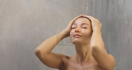 Téléchargez les photos : Spa beauty portrait of young adult woman taking shower washing her hair, splashing water with closed eyes standing on light gray loft background. High quality photo - en image libre de droit