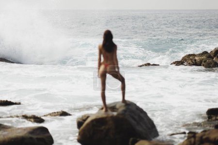 Foto de Escena extrema épica de grandes olas oceánicas estrellándose en la costa rocosa frente a la modelo de playa bikini. Foto de alta calidad - Imagen libre de derechos