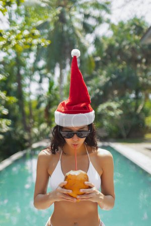 Foto de Mujer joven divertida celebrando Navidad y Año Nuevo en un resort tropical con un sombrero de Santa Claus, bikini bebiendo coco - Imagen libre de derechos