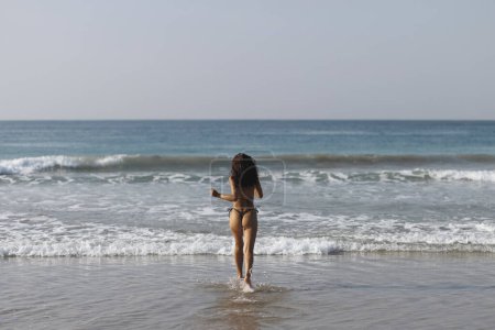 Foto de Feliz bikini mujer de vacaciones de playa corriendo al agua del océano en sensación de libertad. Felicidad estilo de vida despreocupado foto con mar y cielo copiar espacio. - Imagen libre de derechos