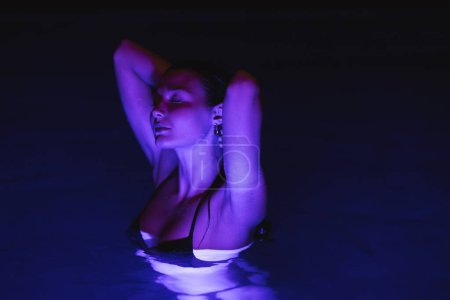 Téléchargez les photos : Détendez-vous belle jeune femme sexy adulte dans un bikini noir relaxant dans la piscine spa. Gros plan du modèle à la mode avec un corps mince parfait nageant la nuit - en image libre de droit