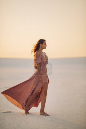 Téléchargez les photos : Promenade romantique mannequin femme à la mode dans le désert en robe rose du soir. Vue latérale de magnifique fille mince à l'extérieur. Photo de haute qualité - en image libre de droit