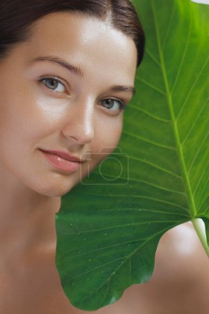 Téléchargez les photos : Cosmétiques naturels soins de la peau produits de beauté ou traitement pour femme. Femme avec un beau visage et une peau faciale saine avec une grande feuille verte tropicale - en image libre de droit