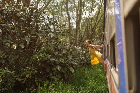 Foto de Viajes y exploración de mujeres turísticas en tren a lugares famosos de Sri Lanka. Viaje turístico por el país tropical. Tour de Kandy a Ella. Atracción extrema, valiente chica pasajera en vestido - Imagen libre de derechos