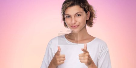 Foto de Retrato de estudio de moda de la mujer feliz de 20 años usa una camiseta blanca que apunta con la cámara de los dedos índice en usted motivando a alentar aislado en el fondo púrpura rosa degradado. Concepto de vida - Imagen libre de derechos