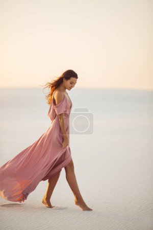 Photo for Walking romantic fashionable woman model in the desert in evening pink dress. Side view of gorgeous slim girl outdoors. High quality photo - Royalty Free Image