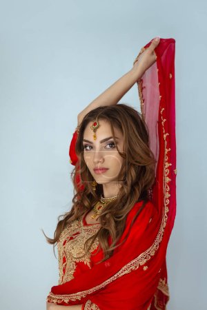 Téléchargez les photos : Portrait de beauté de fille indienne en sari nuptial rouge posant en studio. Jeune femme hindoue modèle bijoux ensemble. Costume indien traditionnel - en image libre de droit