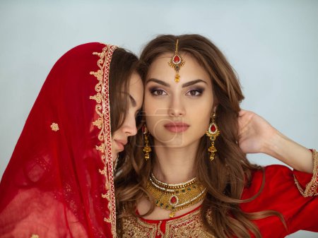 Téléchargez les photos : Portrait de beauté de deux filles indiennes en sari nuptial rouge posant en studio. Jeune hindou femmes modèles bijoux ensemble. Costume indien traditionnel - en image libre de droit