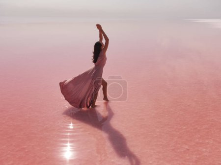 Foto de Pink lake woman. A girl in a pink dress sits on the salty shore of a pink lake and poses for a souvenir photo, creating lasting memories. High quality photo - Imagen libre de derechos