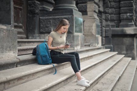 Photo for Young woman sitting on the stairs of a school, uses a smartphone - Royalty Free Image