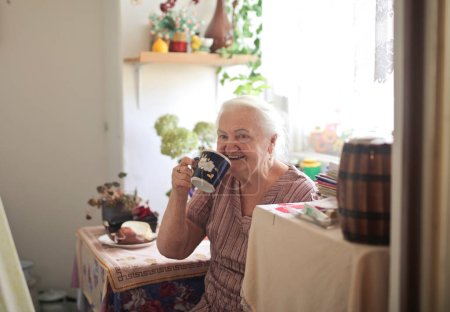 Photo for Elderly lady drinks a cup of tea in the kitchen - Royalty Free Image