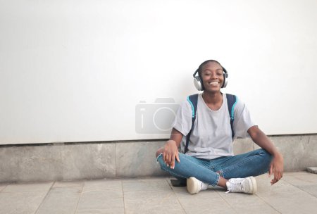 Photo for Young woman sitting with her back to a wall listens to music - Royalty Free Image
