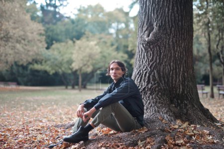 Photo for Portrait of young man sitting near a tree in a park - Royalty Free Image