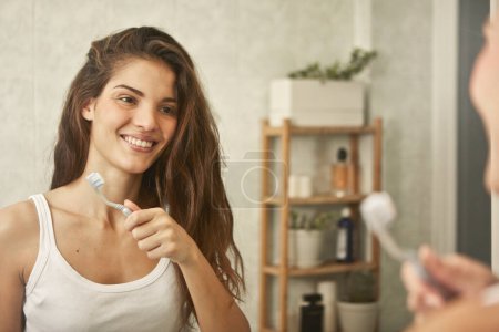 Téléchargez les photos : Portrait de jeune femme dans le miroir sur le point de se brosser les dents - en image libre de droit