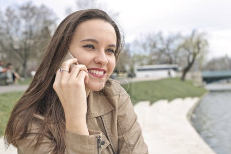 Photo for Young woman in a park speaks on the phone - Royalty Free Image
