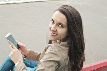 Foto de Mujer joven sentada en un banco utiliza un teléfono inteligente - Imagen libre de derechos