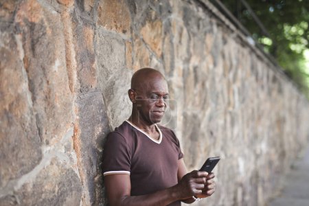 Foto de Hombre adulto apoyado contra una pared utiliza un teléfono inteligente - Imagen libre de derechos