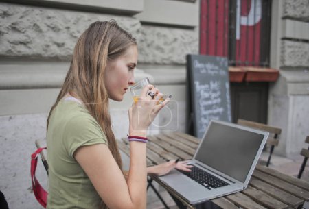 Foto de Mujer joven en un café al aire libre utiliza una computadora - Imagen libre de derechos