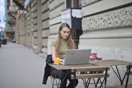 Foto de Mujer joven en un café al aire libre utiliza una computadora - Imagen libre de derechos