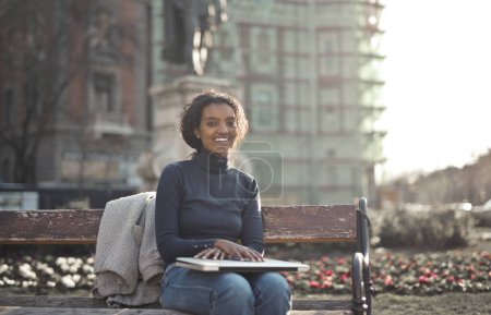 Téléchargez les photos : Jeune femme assise sur un banc avec un ordinateur portable à la main - en image libre de droit