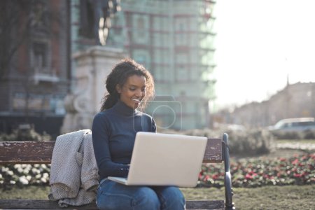Photo for Young woman sitting on a bench uses a laptop - Royalty Free Image