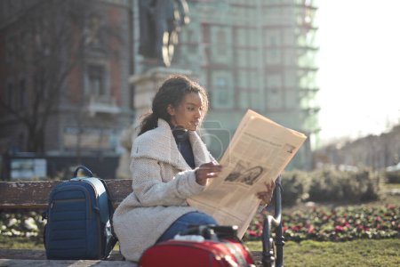 Photo for Young woman sitting on a bench reads a newspaper - Royalty Free Image