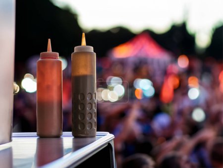 A Pair Of Squeezy Bottles At A Food Truck At A Music Festival Or Concert At Dusk, With Copy Space