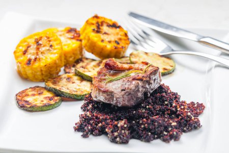 Téléchargez les photos : Steak de porc grillé aux courgettes et maïs servi avec du quinoa noir - en image libre de droit