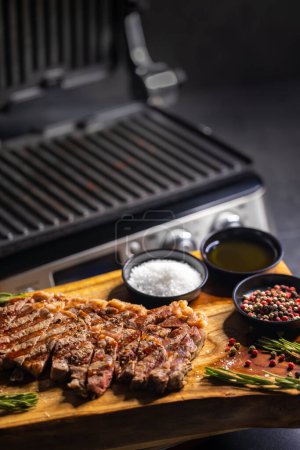 Téléchargez les photos : Steak de seigle sur planche de bois avec épices et grill électrique - en image libre de droit