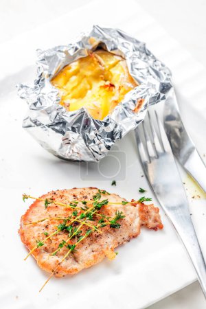 Photo for Poulry steak with baked potato in aluminum foil - Royalty Free Image