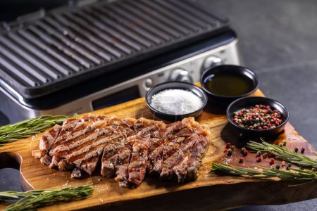 Photo for Ribeye steak on wooden board with spices and electric grill - Royalty Free Image