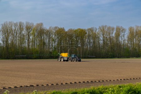 Foto de Tractor with sprayer during spring work on the field - Imagen libre de derechos